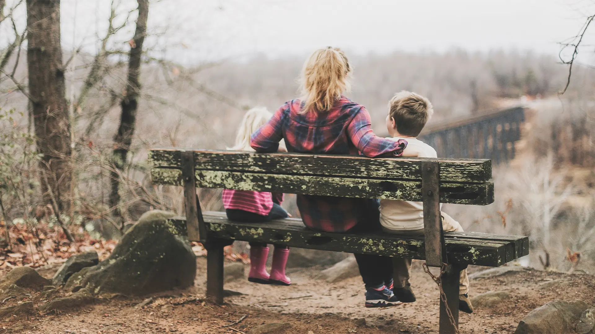 Frau mit zwei Kindern auf einer Bank im herbstlichen Park – Rückenansicht. Symbolbild für familiäre Geborgenheit und starke Abwehrkräfte.