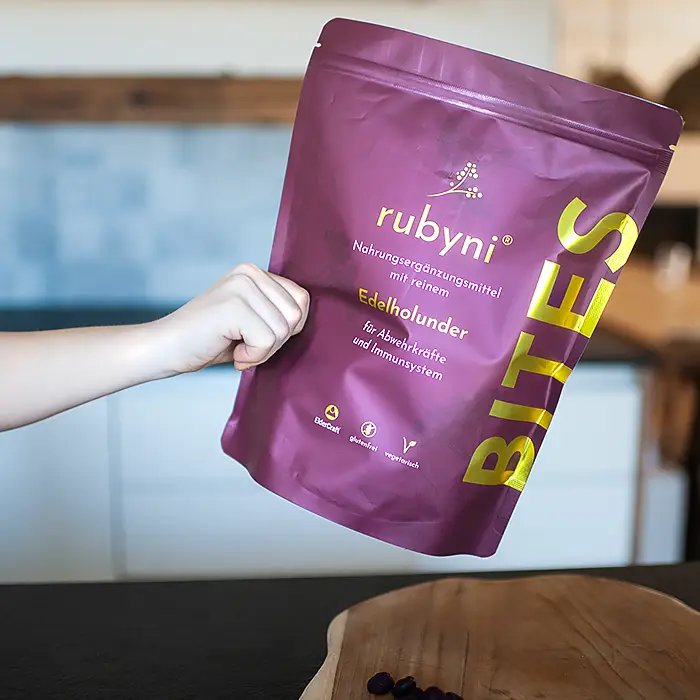 rubyni® BITES Edelholunder für ein starkes Immunsystem bei Kindern Kinderhand hält dunkelroten rubyni® BITES Edelholunder-Beutel
