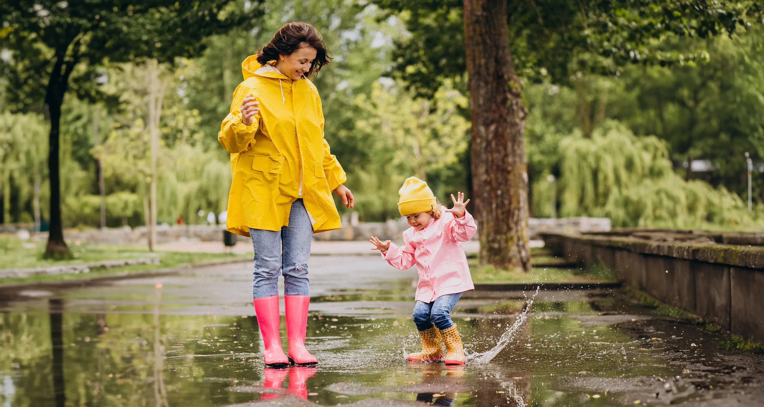 Gestärktes Immunsystem – spielen bei Regen kein Problem Mutter mit springendem Kleinkind in einer Wasserpfütze an einem regnerischen Tag