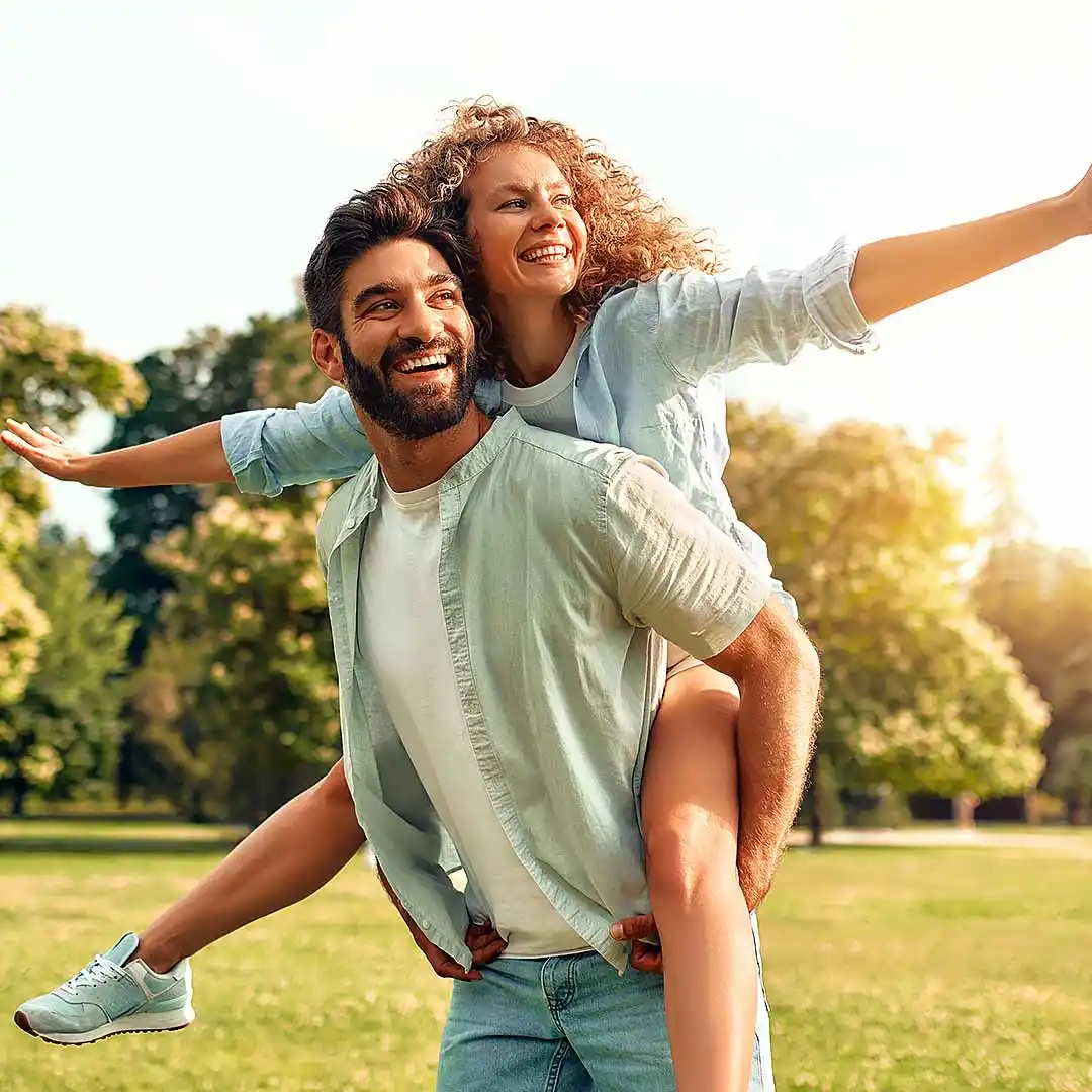 rubyni® CaMag Mineralstoffe unterstützt gesunde Haut, Haare und Nägel lachender Mann trägt lachende Frau auf dem Rücken in einem Park im Sommer bei Sonnenschein
